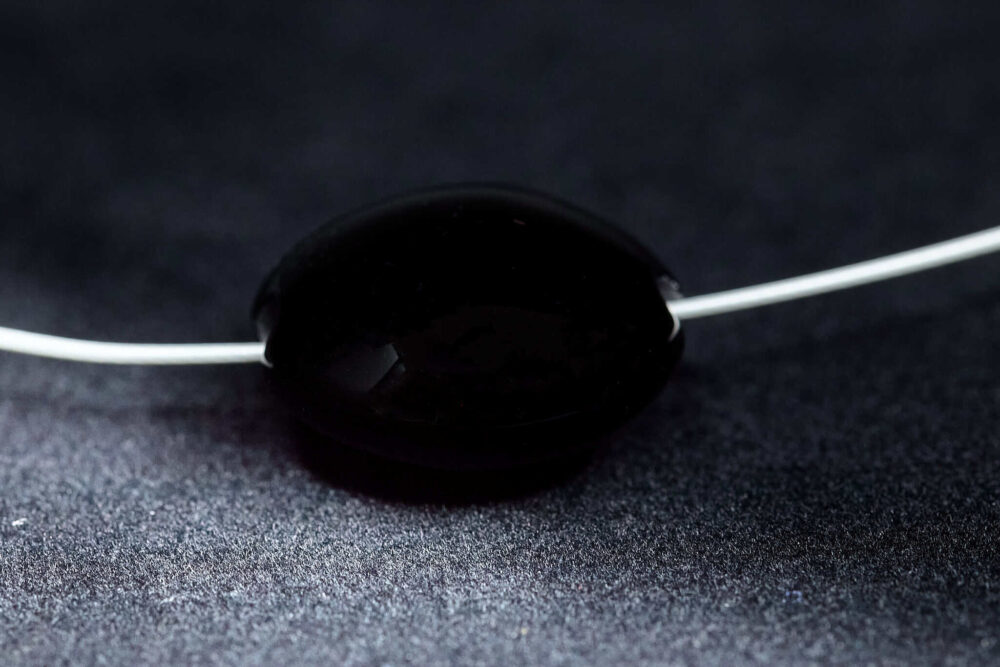Große handgefertigte Lampwork-Linsenperle in Schwarz als Wechselperle auf einem Edelstahl-Halsreif.