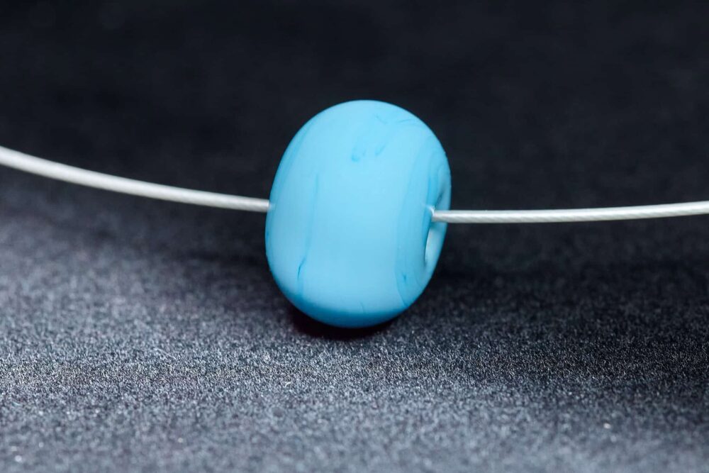 Kleine handgefertigte Lampwork-Glasperle in Himmelblau als Wechselperle auf einem Edelstahl-Halsreif.